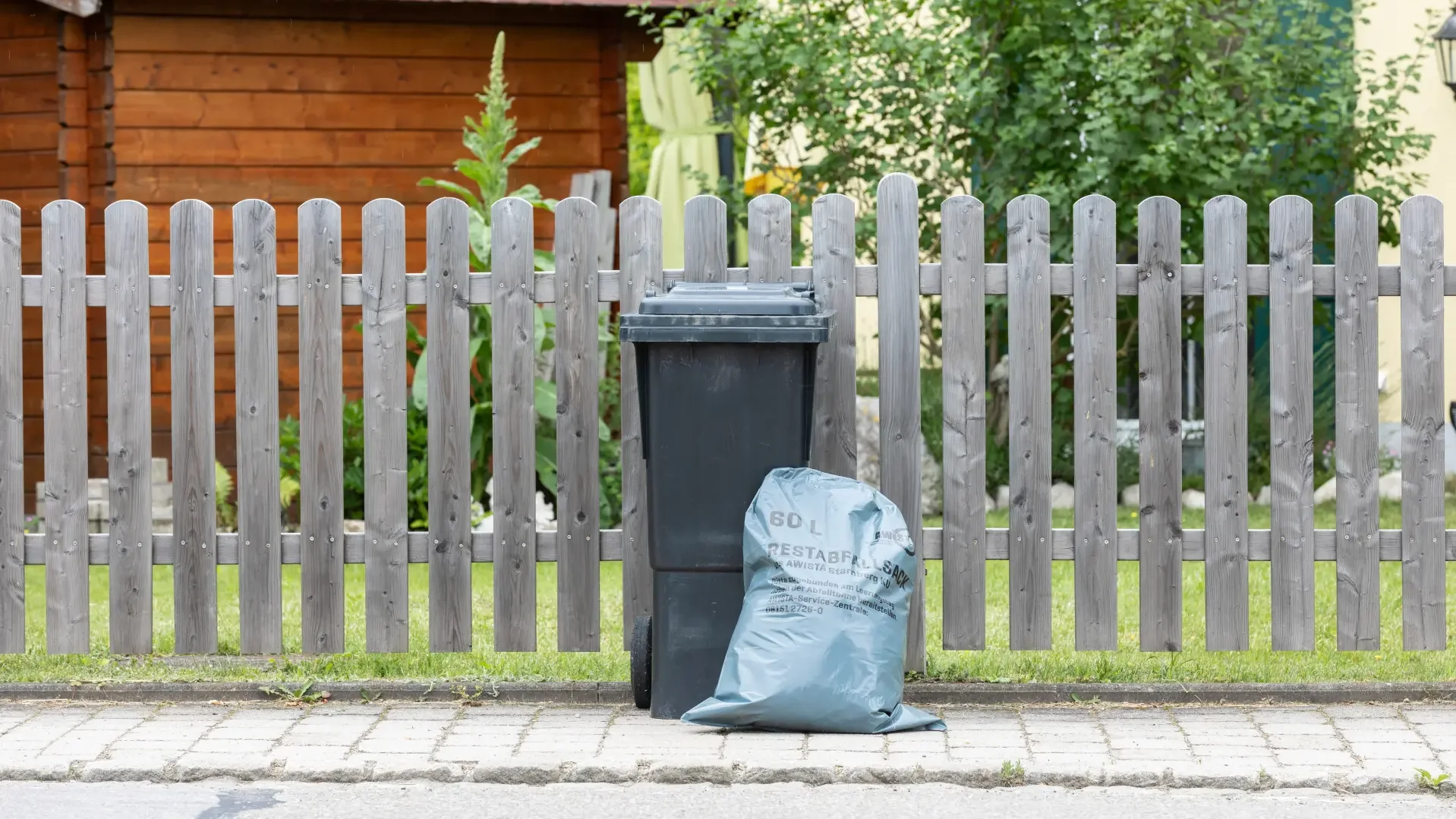 Restmülltonnen und Restmüllsack vor Gartenzaun