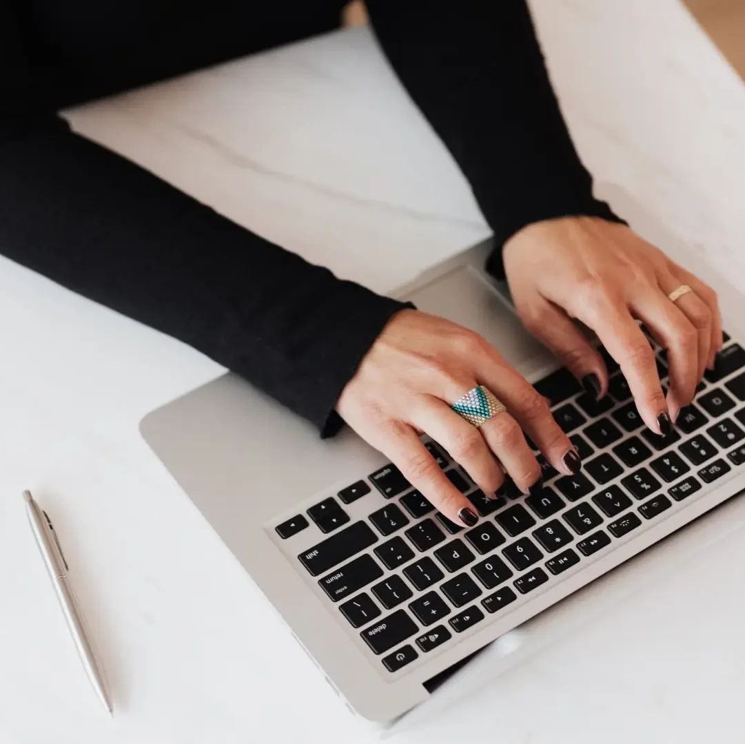 Schreibstisch-Ansicht von oben, Person schreibt am Laptop, Handy und Stift liegen auf Tisch