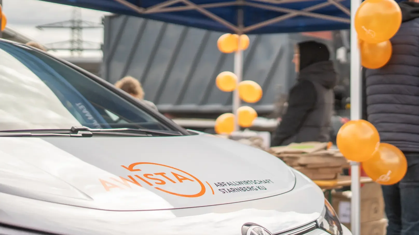 Fahrzeug von AWISTA-Starnberg mit Logo auf der Motorhaube vor einem Pavillon mit orangenen Ballons