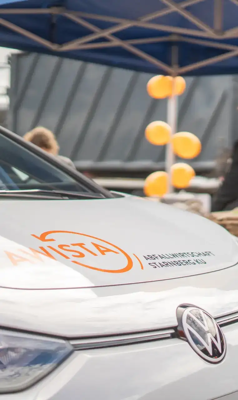 Fahrzeug von AWISTA-Starnberg mit Logo auf der Motorhaube vor einem Pavillon mit orangenen Ballons