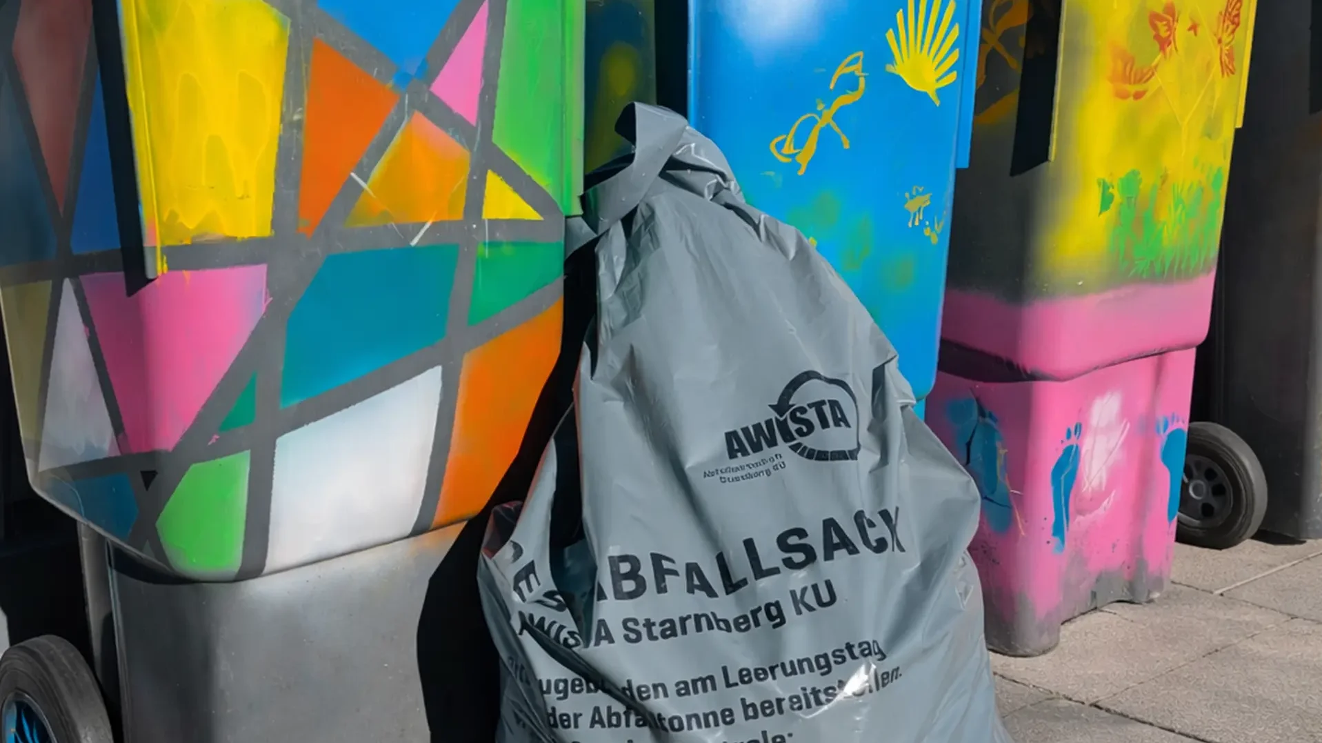 Restmüllsack vor bunt bemalten Mülltonnnen